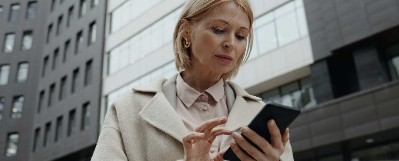 Femme consultant son smartphone devant des immeubles de bureaux